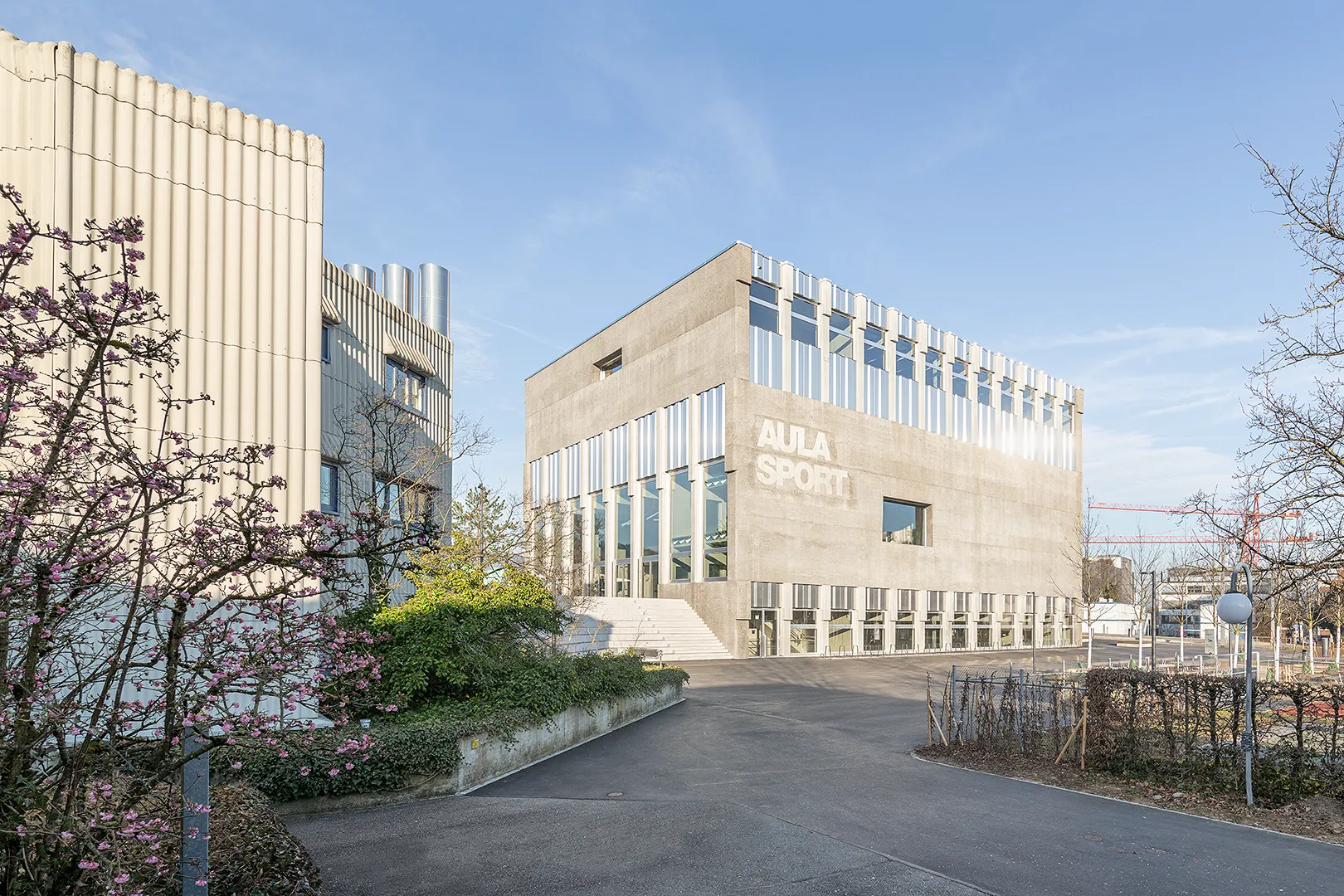 Architecture Photography of a modern brutalist-style school buildings, Kantonsschule Limmattal, featuring light gray-brown recyled-concrete facades and rectangular windows on the exterior, designed by PENZISBETTINI in Urdorf, Zürich.
