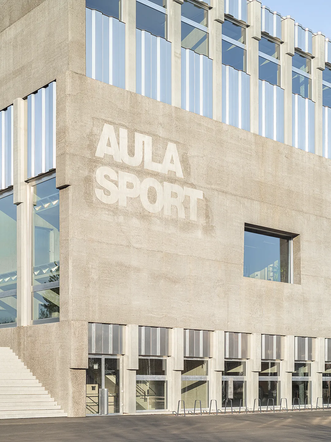 Architecture Photography of a modern brutalist-style school buildings, Kantonsschule Limmattal, featuring light gray-brown recyled-concrete facades and rectangular windows on the exterior, designed by PENZISBETTINI in Urdorf, Zürich.