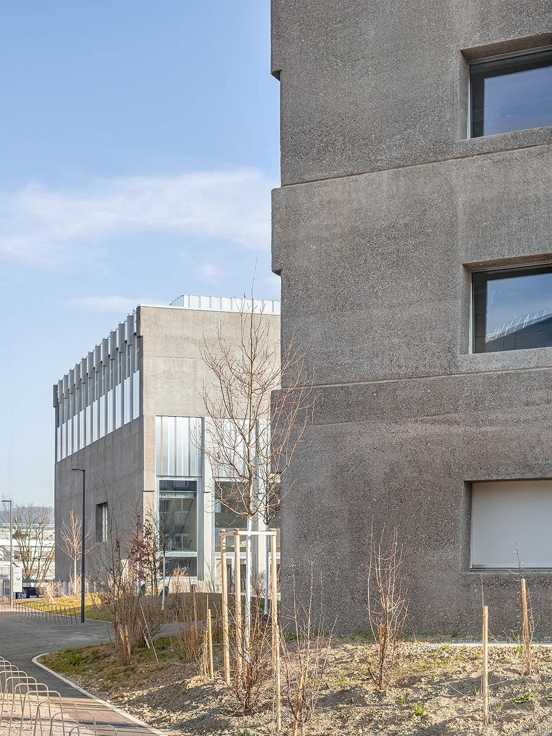 Architecture Photography of a modern brutalist-style school buildings, Kantonsschule Limmattal, featuring light gray-brown recyled-concrete facades and rectangular windows on the exterior, designed by PENZISBETTINI in Urdorf, Zürich.