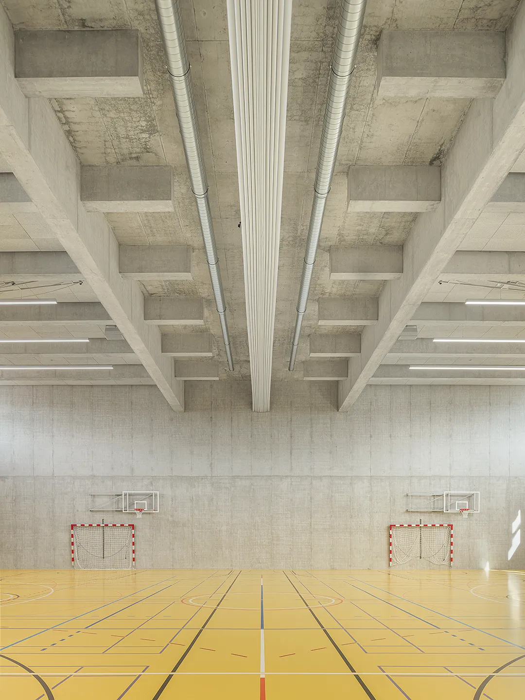 Architecture Photography of a modern brutalist-style school buildings, Kantonsschule Limmattal, featuring light gray-brown recyled-concrete facades, interior view of the sportshall with prefabricated concrete structure by ingegneri pedrazzini guidotti, designed for PENZISBETTINI in Urdorf, Zürich.