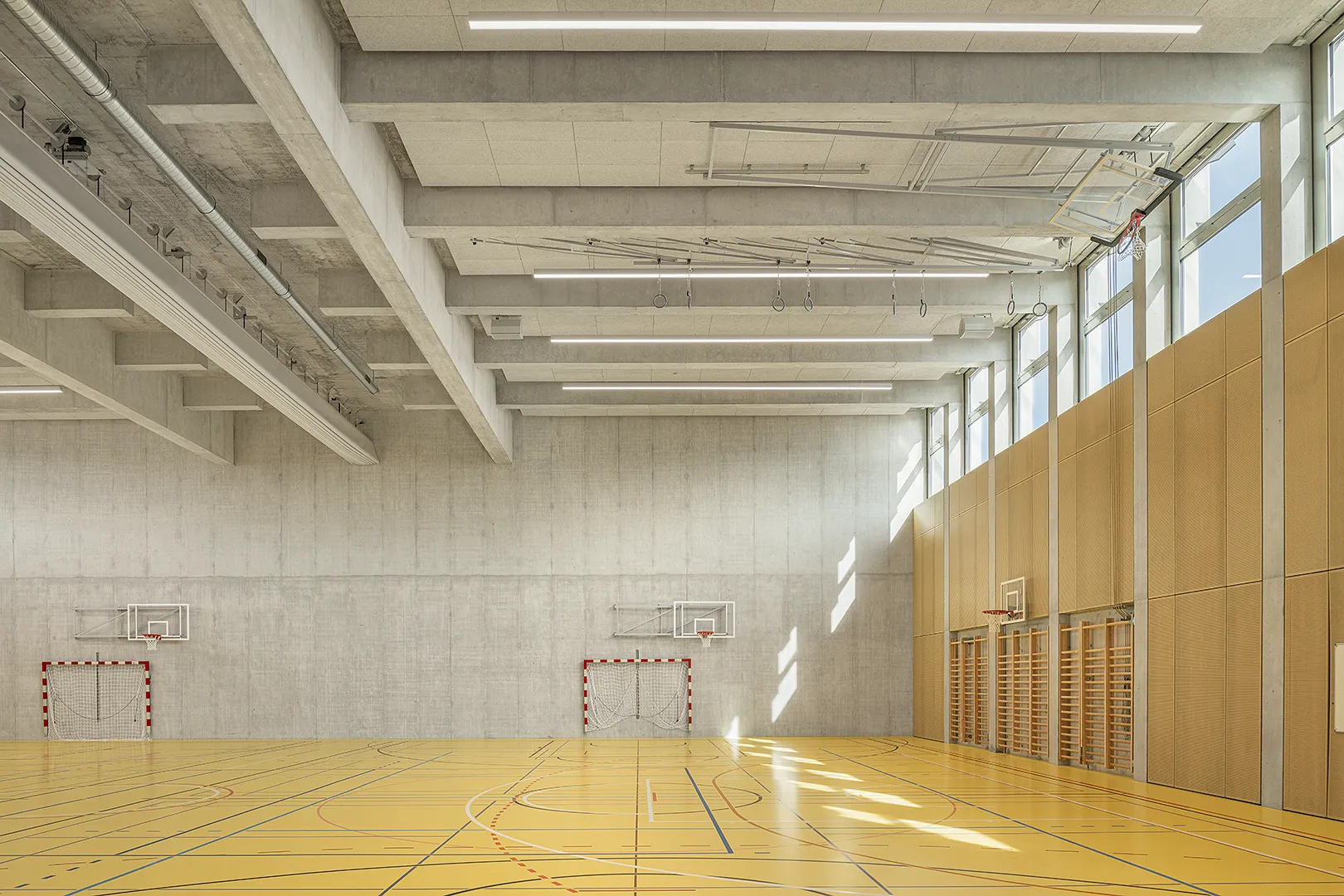 Architecture Photography of a modern brutalist-style school buildings, Kantonsschule Limmattal, featuring light gray-brown recyled-concrete facades, interior view of the sportshall with prefabricated concrete structure by ingegneri pedrazzini guidotti, designed for PENZISBETTINI in Urdorf, Zürich.